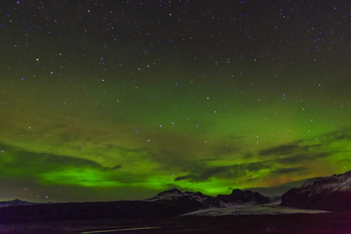 Green aurora stretching across the night sky above a dark mountain ridge in Iceland